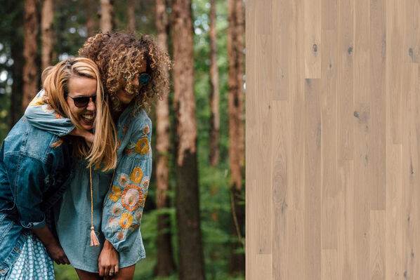 Zwei Frauen halten sich lachend im Arm, im Wald und daneben ist ein natürlicher Parkettboden eingeblendet.