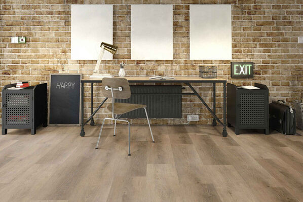 Büro mit Vinylboden, der nach echtem Holzfußboden aussieht. Darauf steht ein Schreibtisch vor einer gemauerten Wand im coolen Industrielook. Über dem Schreibtisch hängen drei Bilder.